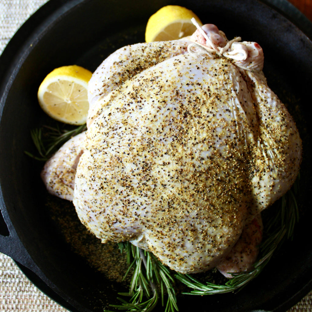 Seasoned whole chicken in a cast iron skillet with rosemary and lemon garnish
