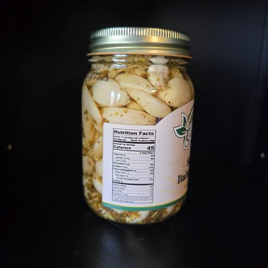 A glass jar filled with sliced garlic cloves in oil with herbs, sealed with a gold metal lid and featuring a white label with a nutrition facts panel, set against a dark background.