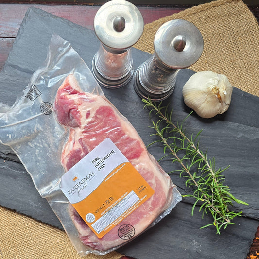 A vacuum-sealed package of raw beef steak with a visible label, arranged on dark gray and beige burlap mats over a distressed red wooden table. A sprig of rosemary, a garlic bulb, and two metal salt/pepper shakers are placed beside it.