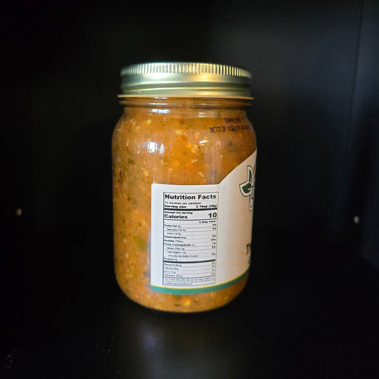 A glass jar filled with chunky orange salsa or guacamole, sealed with a gold metal lid and featuring a white label with nutrition facts, set against a dark black background.