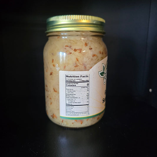 A glass jar of shredded pale beige food with visible orange flecks, sealed with a gold metal lid and a white label showing nutrition facts, photographed on a dark background.
