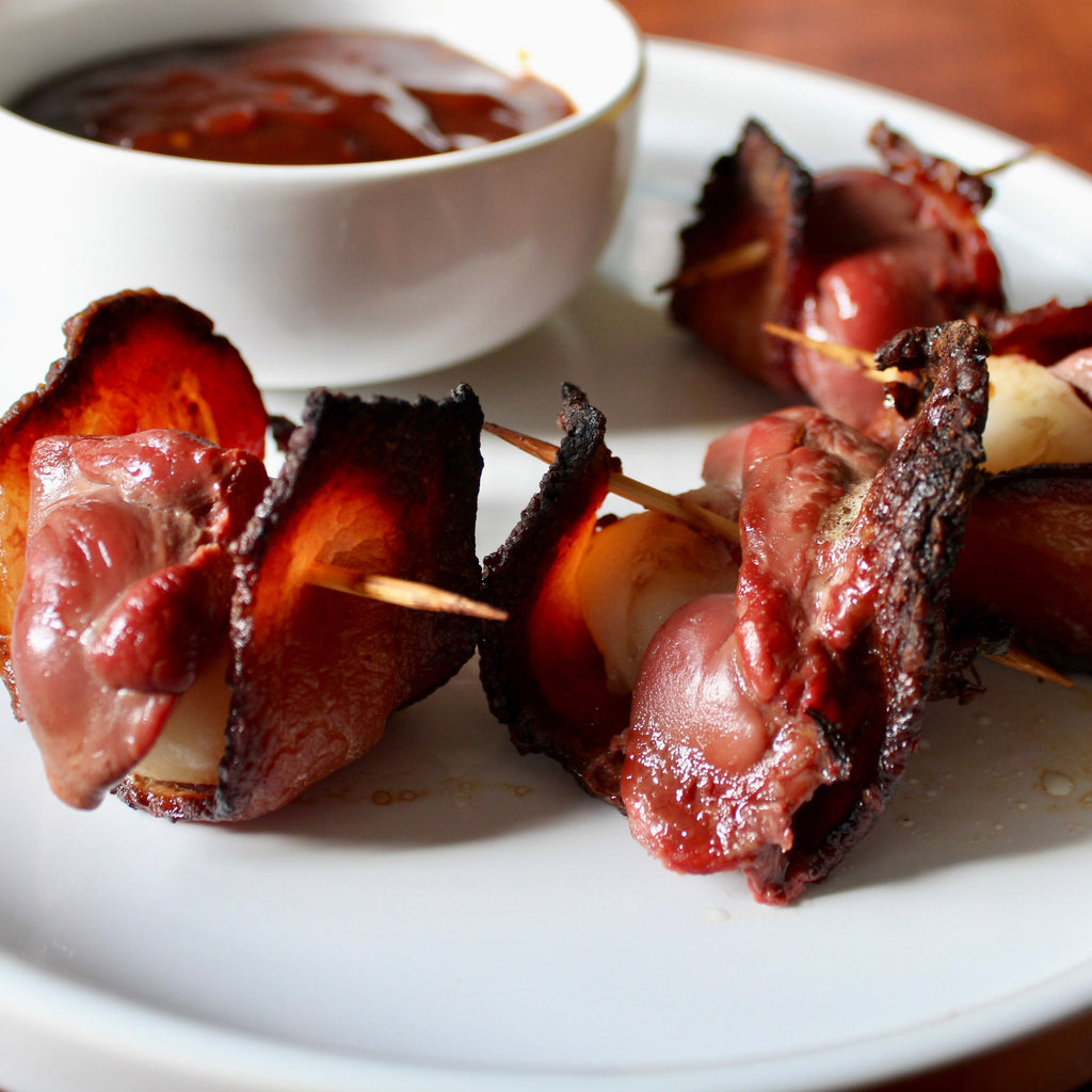 Bacon-wrapped livers on a plate with a side of dipping sauce.