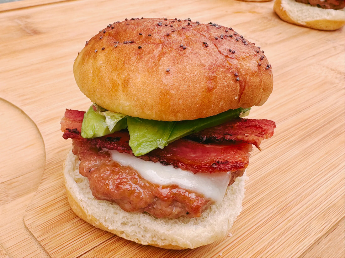 Mini turkey burger with avocado, bacon, and cheese on cutting board