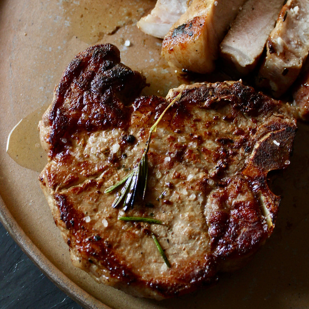 Reverse seared pork chop with rosemary on a beige plate