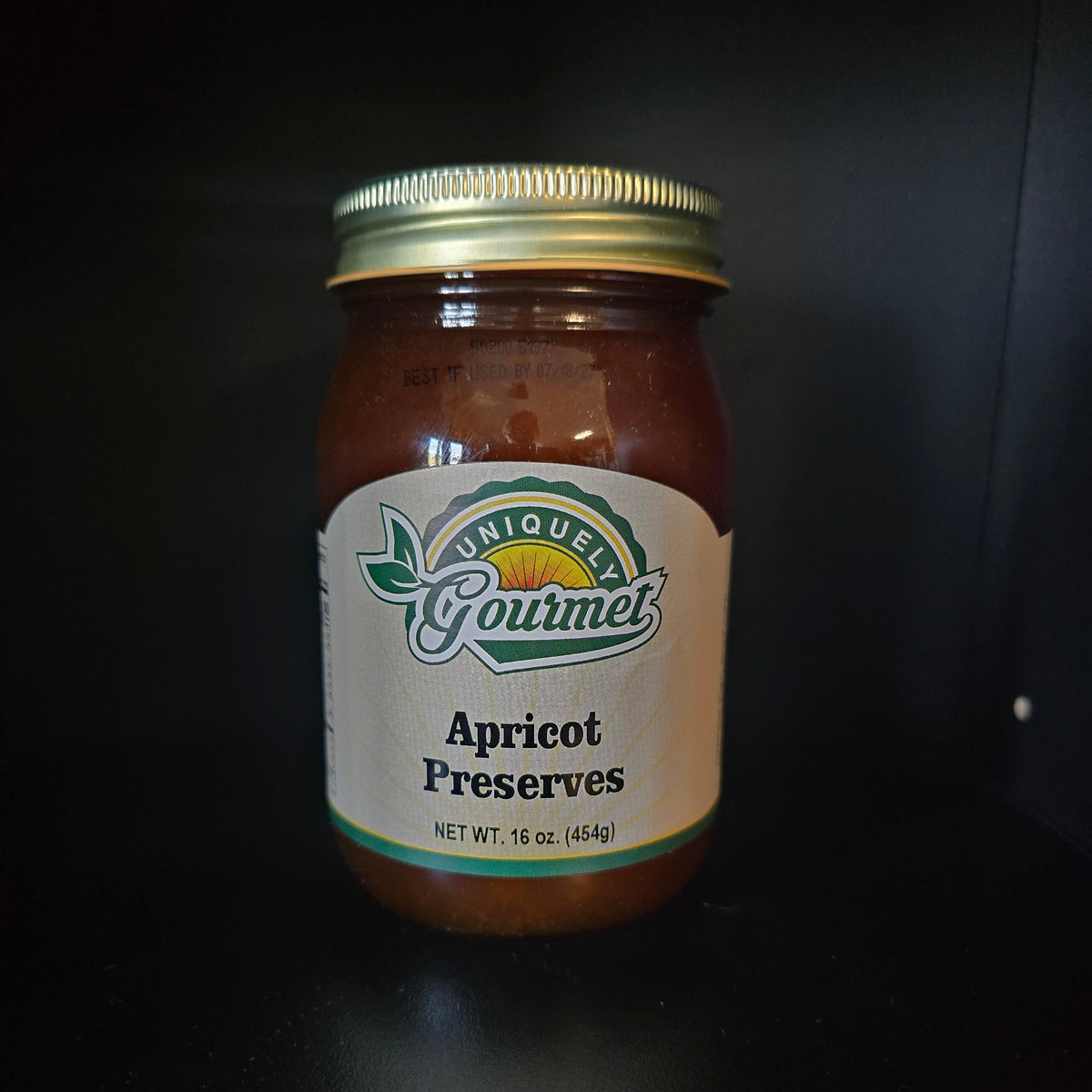 A jar of uniquely Gourmet Apricot Preserves with a gold metal lid and a white label, set against a dark black background.