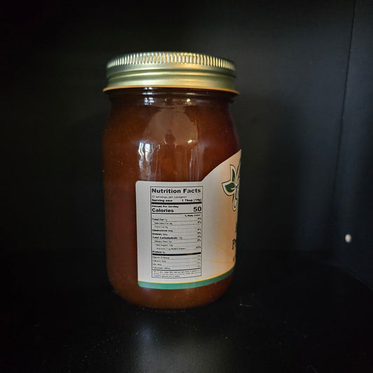 A glass jar filled with amber-brown honey, featuring a gold metal lid and a partially visible cream-colored label, set against a dark background.