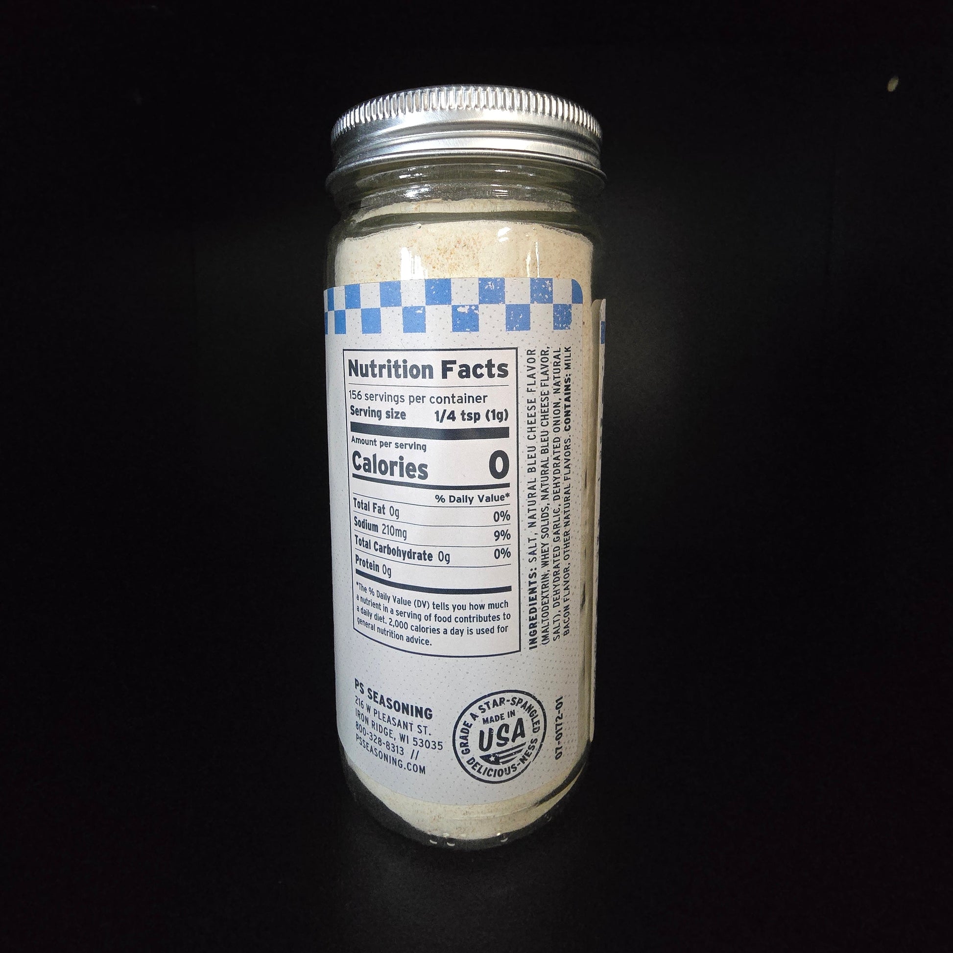A glass jar with a silver metal lid and a white label featuring a blue checkered pattern and nutrition facts, set against a solid black background.