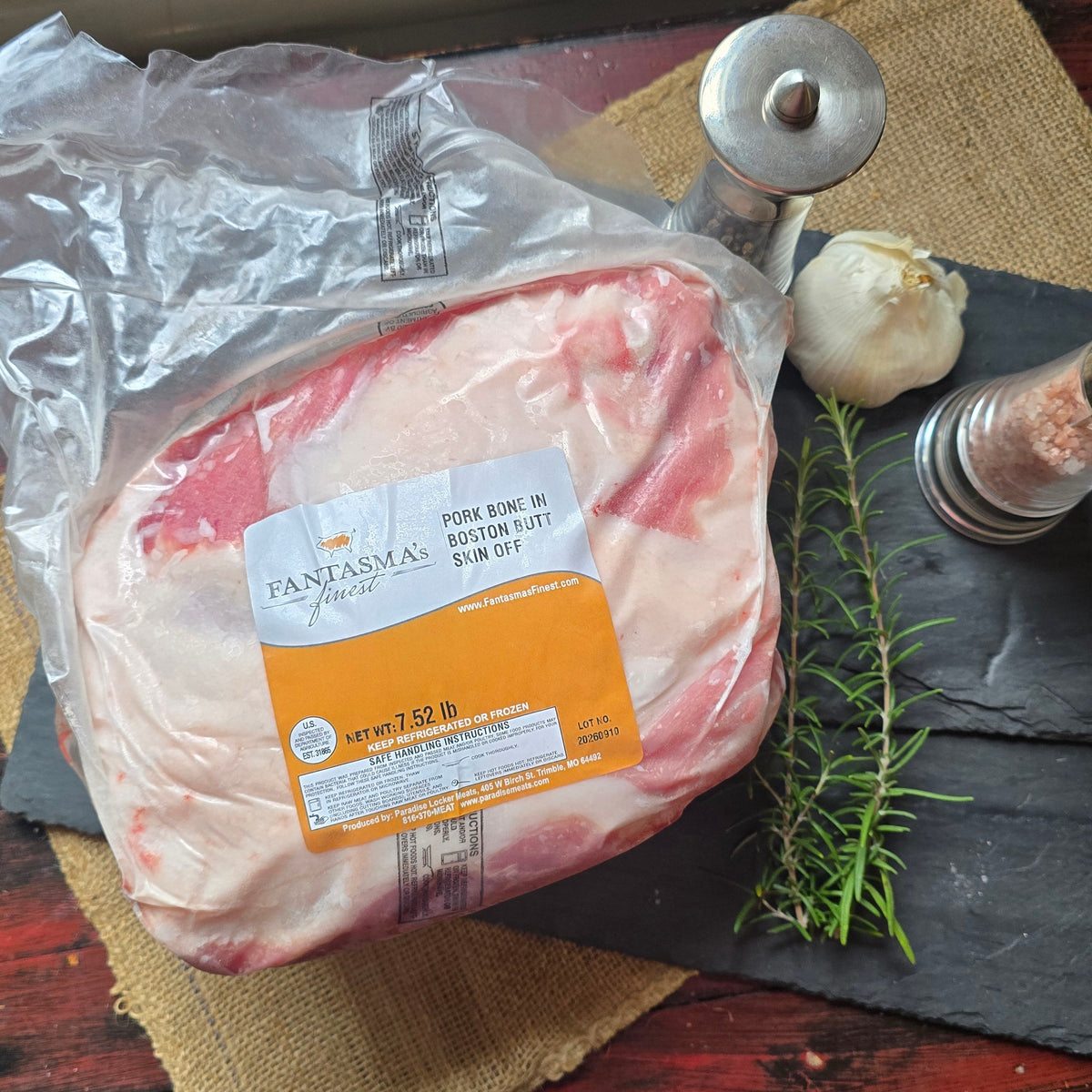 A package of Panamea 2024 Rimón 18% fat beef short rib, styled on a rustic red wooden table with burlap, a black slate board, a sprig of rosemary, a garlic bulb, and salt and pepper mills.