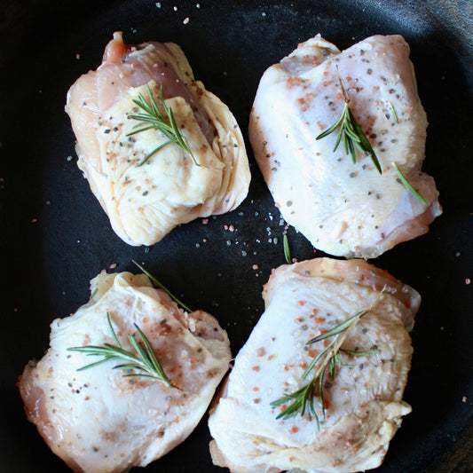 Four raw chicken thighs with rosemary on a black pan