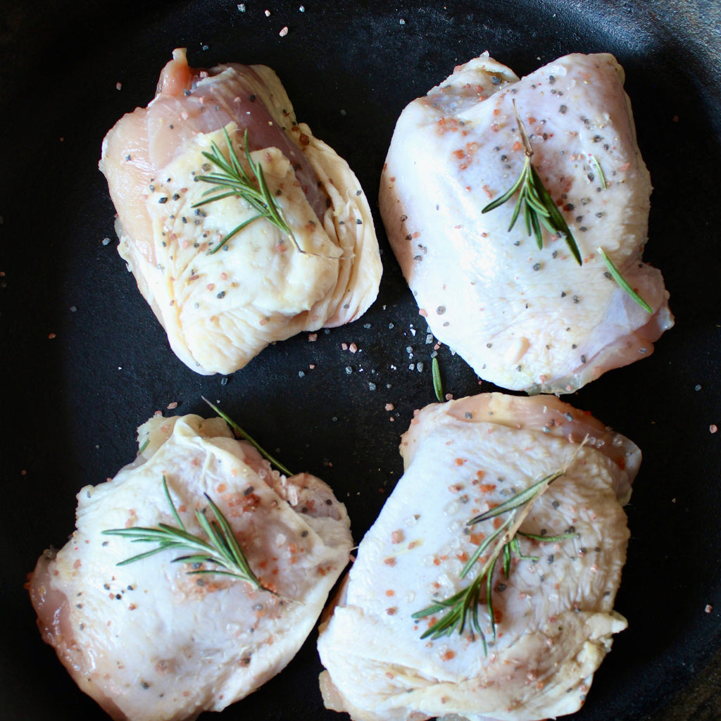 Four raw chicken thighs with rosemary on a black pan