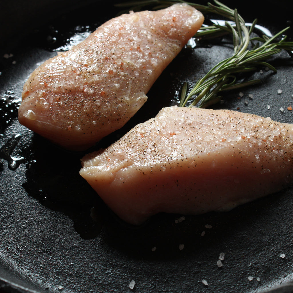 Seasoned raw chicken breast in a cast iron skillet with a sprig of rosemary