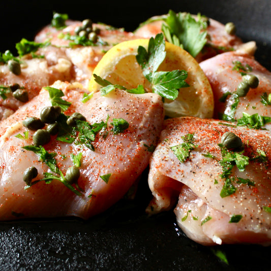6 seasoned boneless chicken thigh pieces with herbs and lemon in a cast iron skillet 
