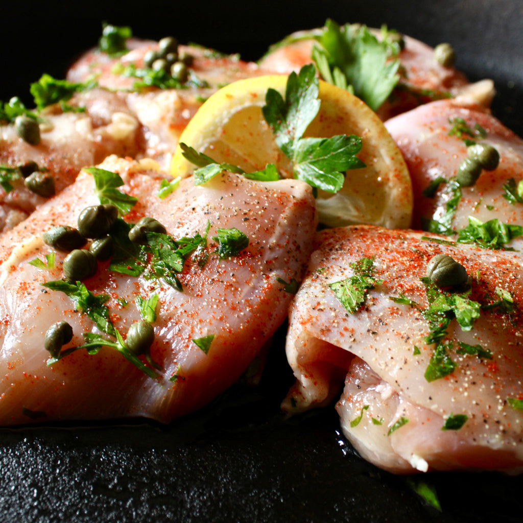 6 seasoned boneless chicken thigh pieces with herbs and lemon in a cast iron skillet 