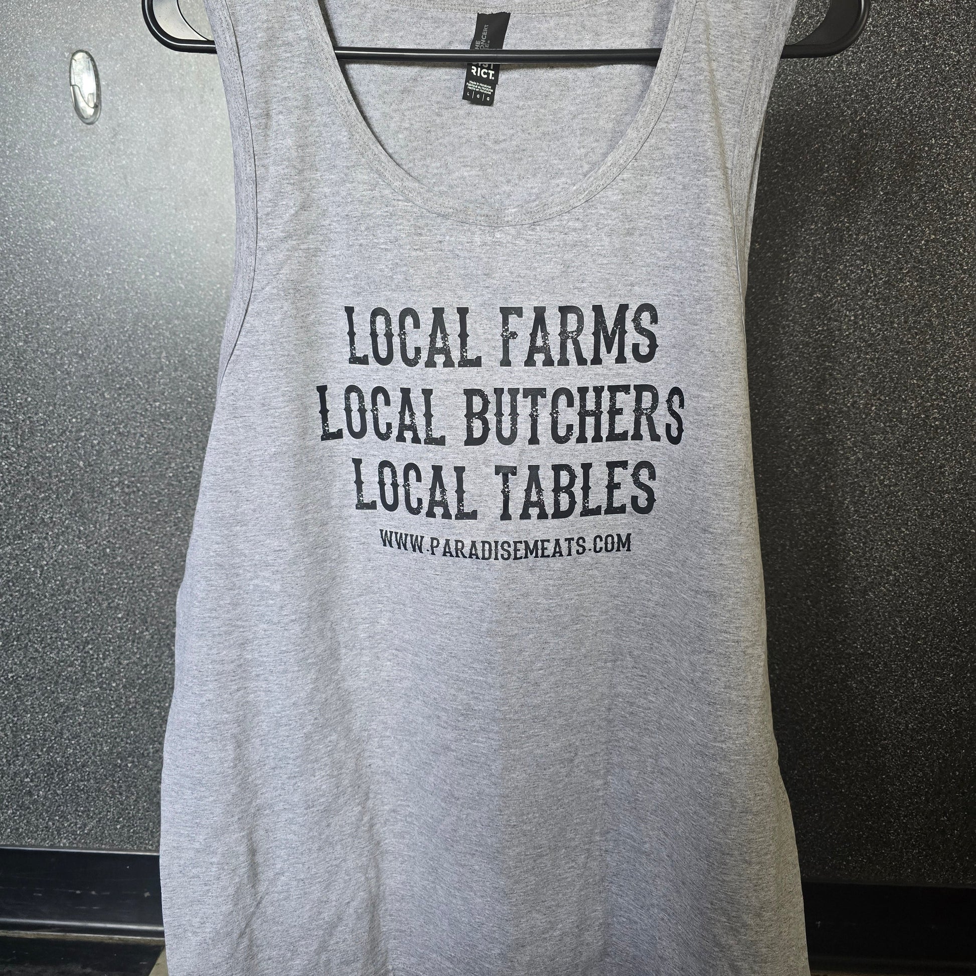 A light heather gray sleeveless tank top hanging on a black hanger, featuring the text 'LOCAL FARMS LOCAL BUTCHERS LOCAL TABLES' and a website URL printed in black on the front.