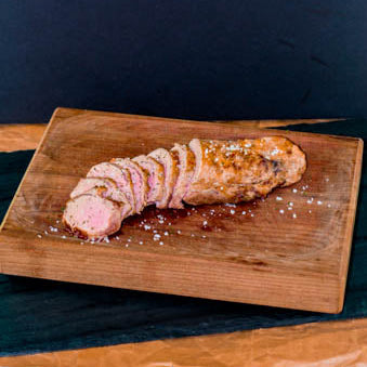 Sliced pork tenderloin on a wooden cutting board with a dark background