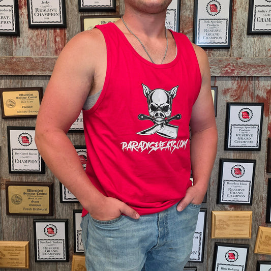 A smiling man wearing a bright red tank top with a skull and crossbones graphic and the word 'PARACOGUSSION' stands in front of a wall covered in framed championship certificates. He is also wearing light blue jeans and dark rubber boots.