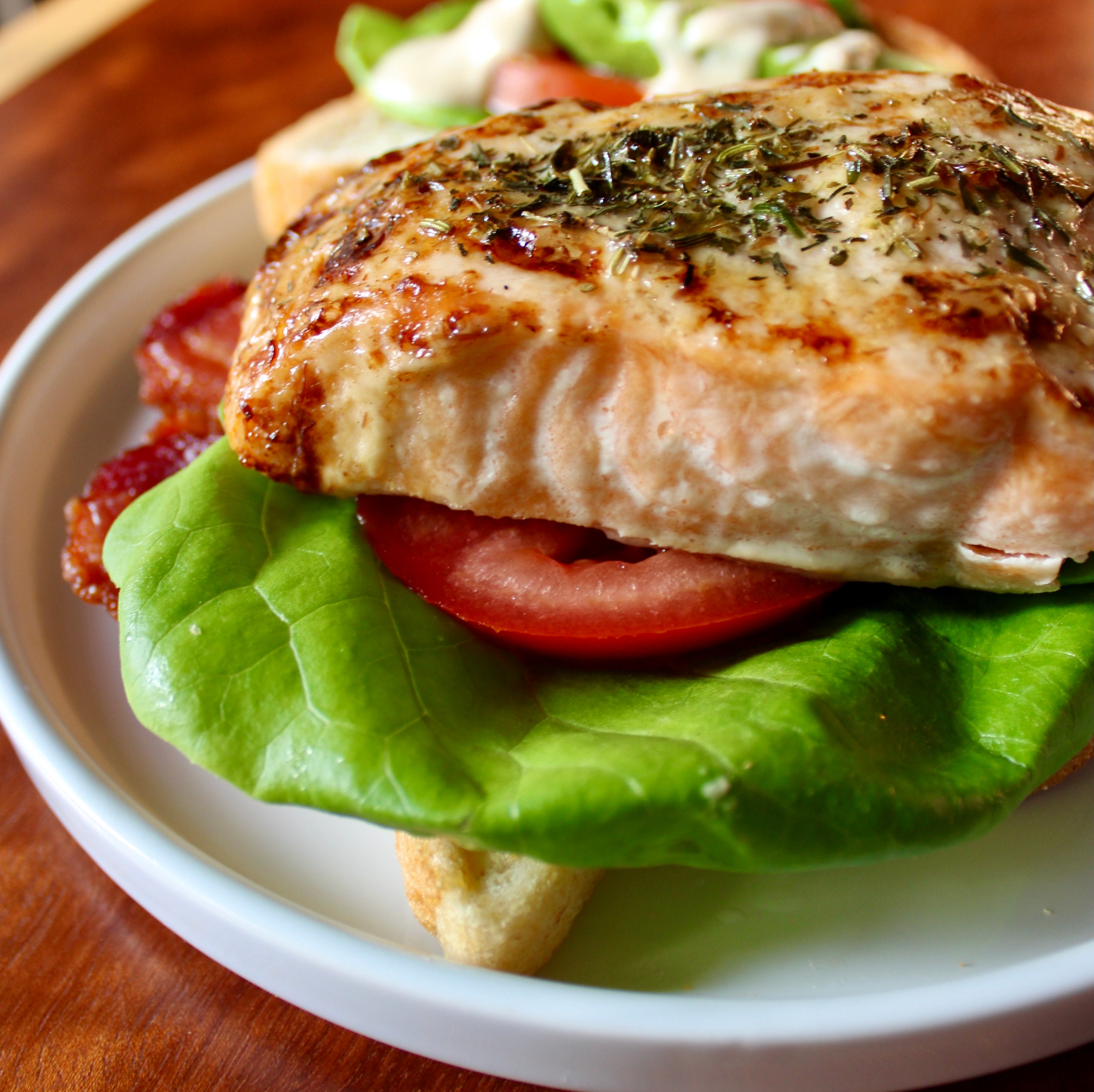Sandwich with salmon, bacon, tomato and lettuce on a white plate