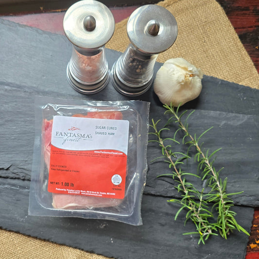 A packaged food product labeled 'Savory' with a red and white label, placed on a dark slate board with a garlic bulb, rosemary sprig, and two metal salt/pepper shakers on a rustic red wooden table with burlap cloth.