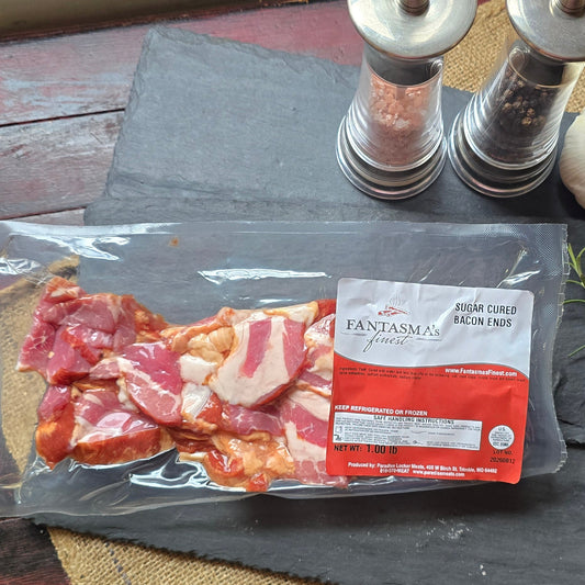 A package of sliced bacon resting on a dark slate board, styled with a sprig of rosemary, a garlic bulb, and two salt and pepper mills on a rustic red wooden table.