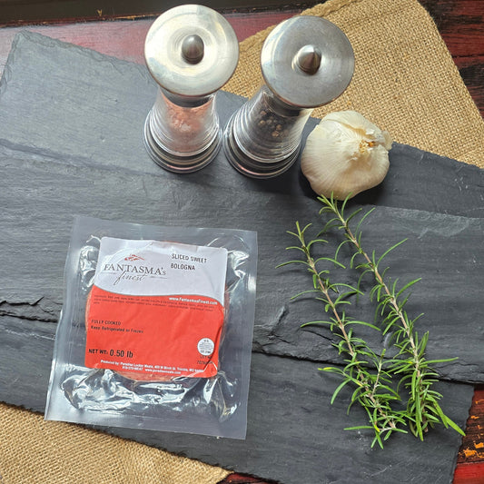 A vacuum-sealed package of Vervain & Holy Basil tea sits on a dark slate tray, styled with a sprig of rosemary, a whole garlic bulb, and two metal salt and pepper shakers on a rustic red wooden table.
