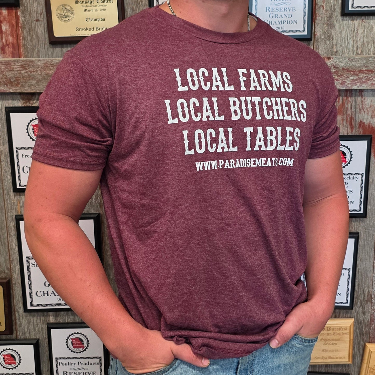 A man wearing a heathered maroon t-shirt with white text that reads 'LOCAL FARMS LOCAL BUTCHERS LOCAL TABLES WWW.PARADISEMEAT.
