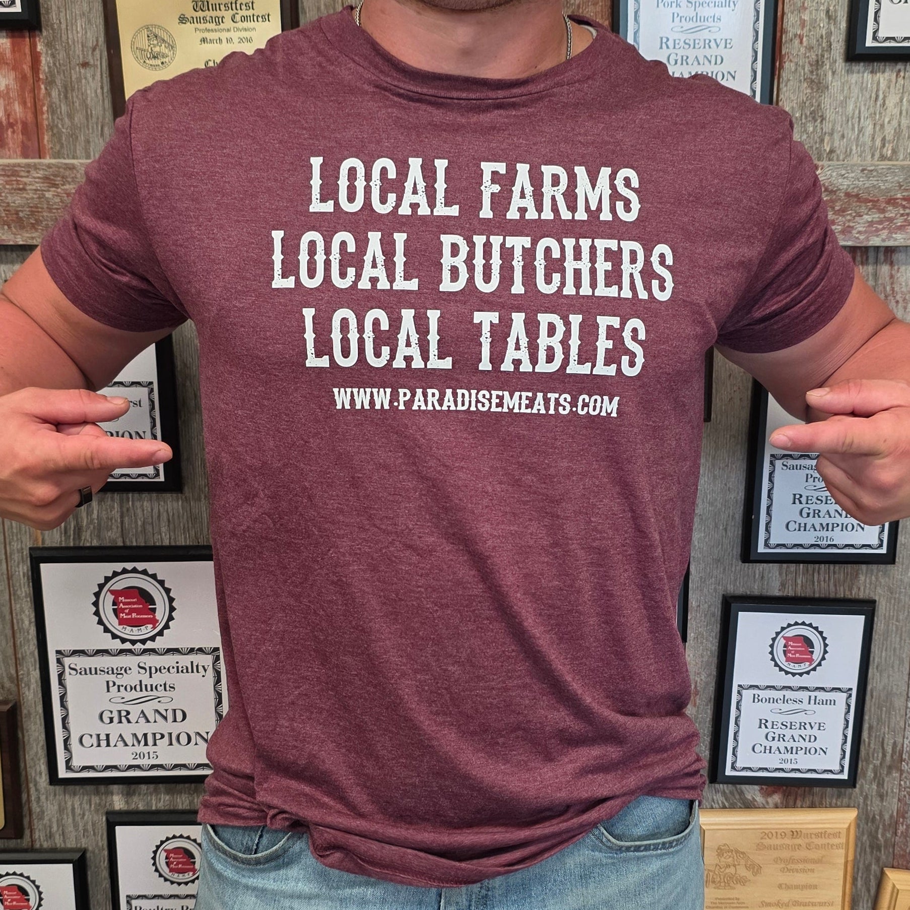 A smiling man wearing a heathered maroon t-shirt with white text that reads 'LOCAL FARMS LOCAL BUTCHERS LOCAL TABLES WWW.FARABONEMEATS.