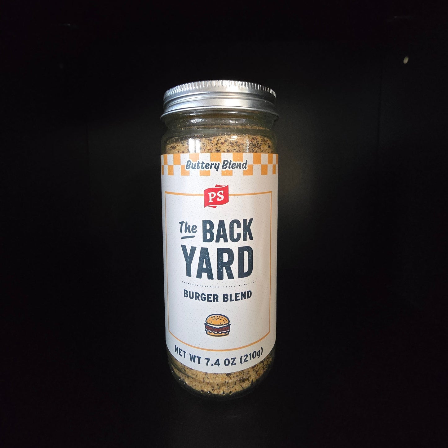 A glass jar of PS Buttery Blend 'The Back Yard' Burger Blend seasoning, set against a solid black background.