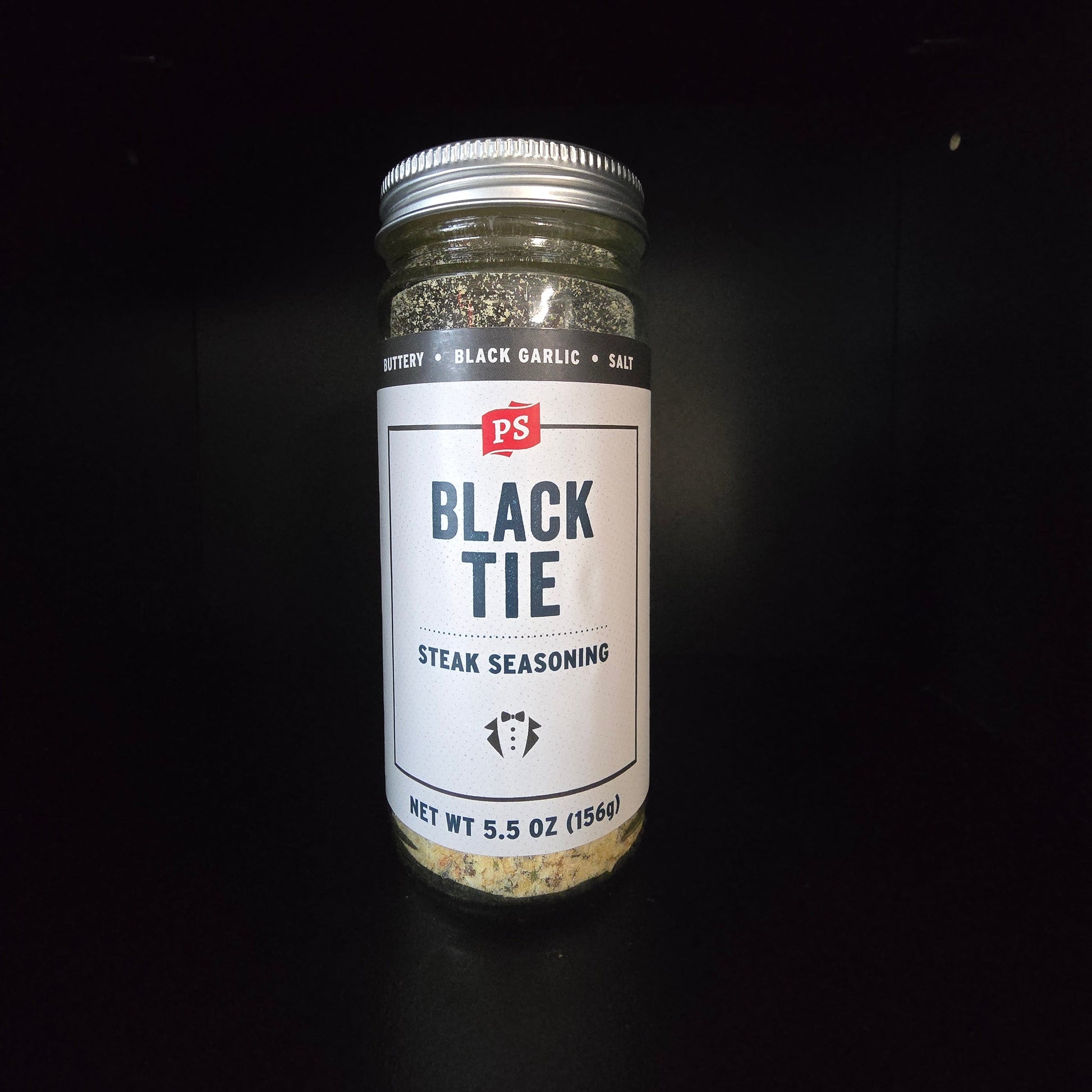 A bottle of Black Tie Steak Seasoning with a white label and silver cap, set against a solid black background.