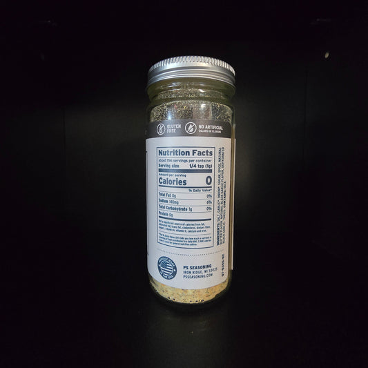 A glass jar of seasoning with a white label and silver lid, standing on a black surface against a black background.