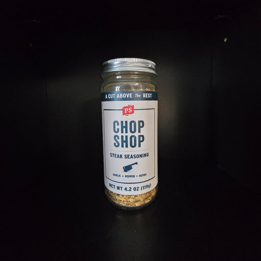 A glass jar of Chop Shop Steak Seasoning with a white label and silver lid, set against a dark black background.