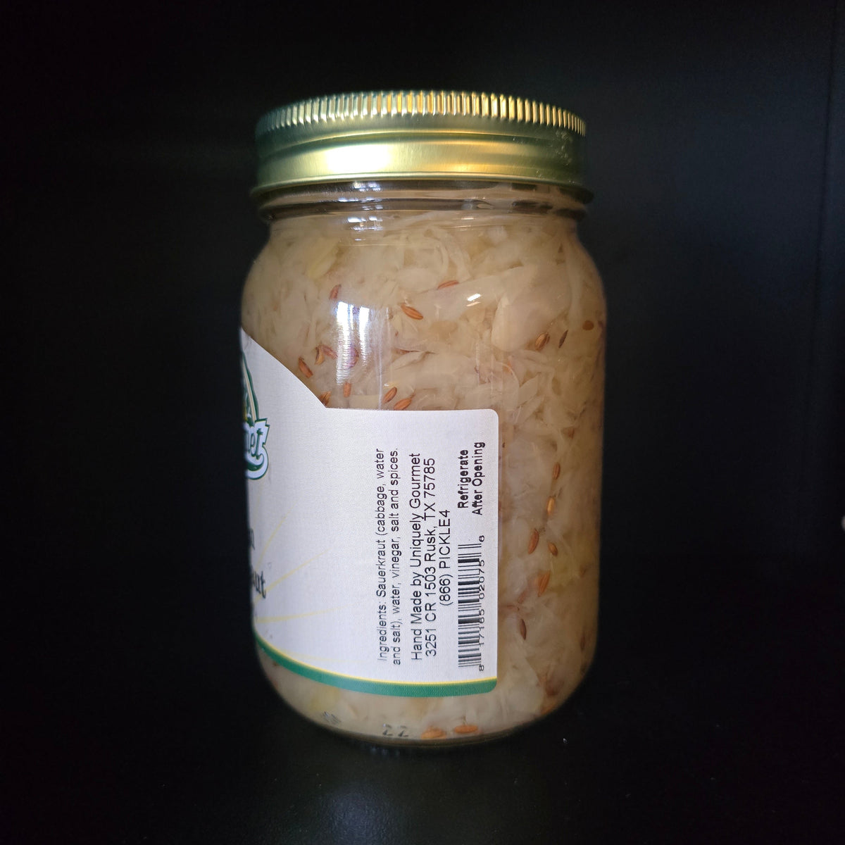 A glass jar of pickled or preserved onions with a gold metal lid and a white label, photographed against a dark black background.