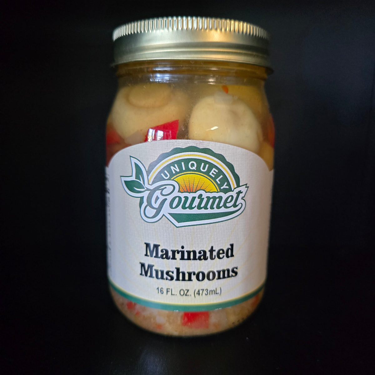 A jar of uniquely gourmet marinated mushrooms with a white label and gold metal lid, set against a dark black background.
