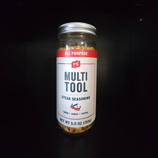 A 5.5 oz glass jar of PS Multi Tool Steak Seasoning with a white and red label, set against a solid black background.