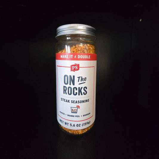 A glass jar of PS On The Rocks Steak Seasoning with a white and red label, set against a solid black background.
