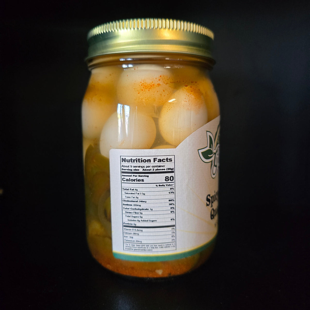 A glass jar of sliced sautéed onions in oil with a gold metal lid, shown against a dark black background. The front label displays a nutrition facts panel and partial branding.