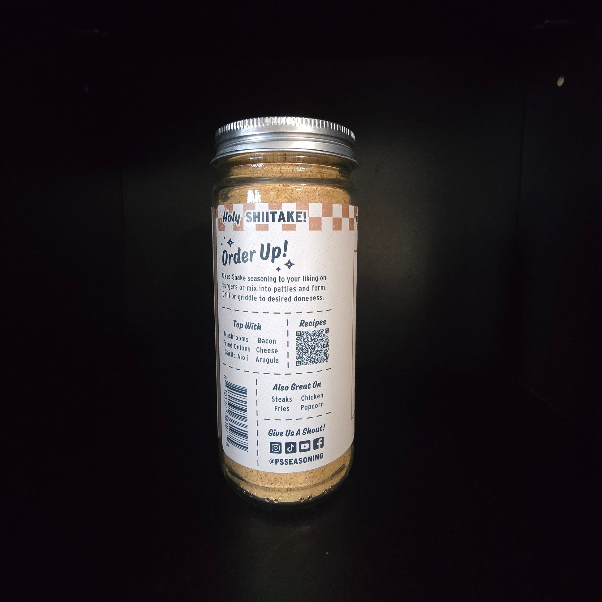 A glass jar of seasoning powder with a silver metal lid and a white label, photographed against a solid black background.